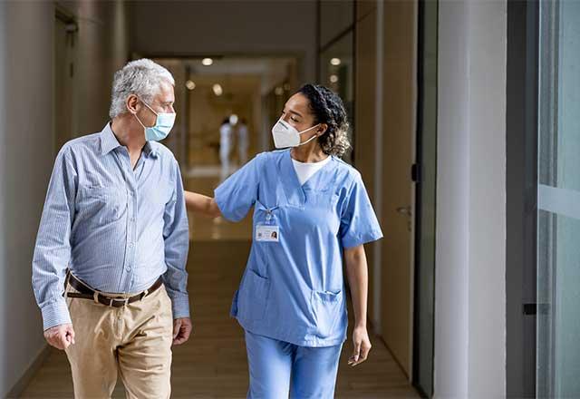 Healthcare provider walking with a patient down a hospital hallway.