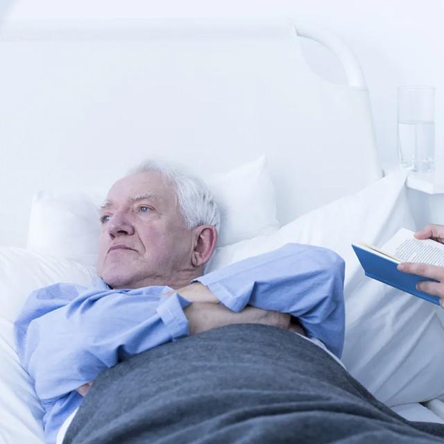 An elderly man lays in his hospital bed pouting