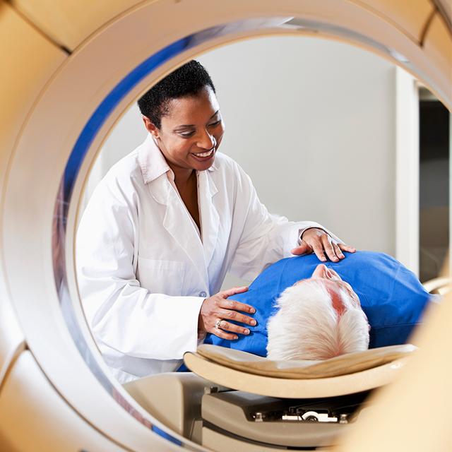 A female doctor helps an elderly male patient in a CAT scan machine.