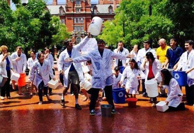 Healthcare providers standing outside with a large water bucketing being poured over one of their heads.